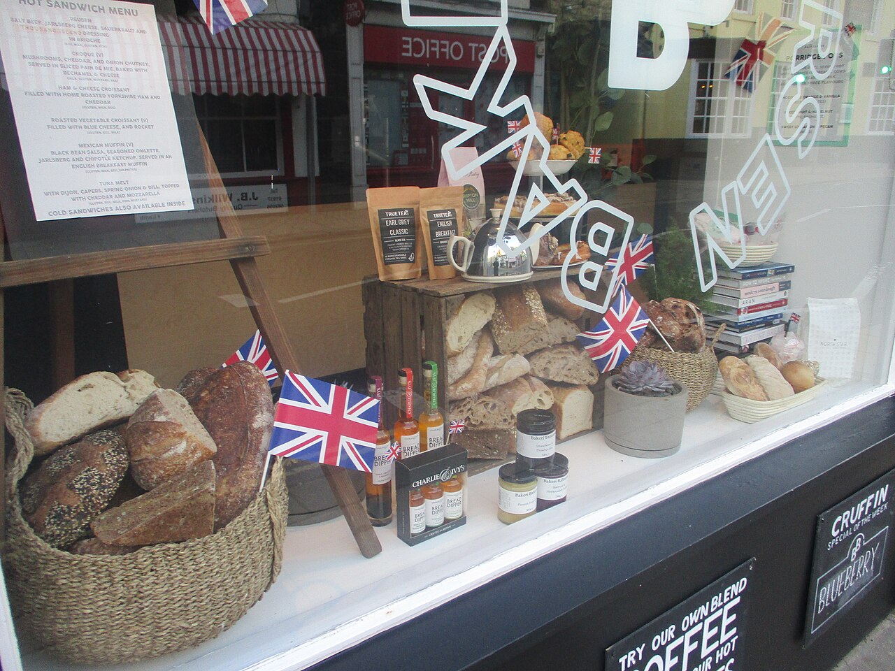Vitrine de boulangerie avec des pains dans des paniers et le nom en lettres de vinyle blanc sur la vitre.