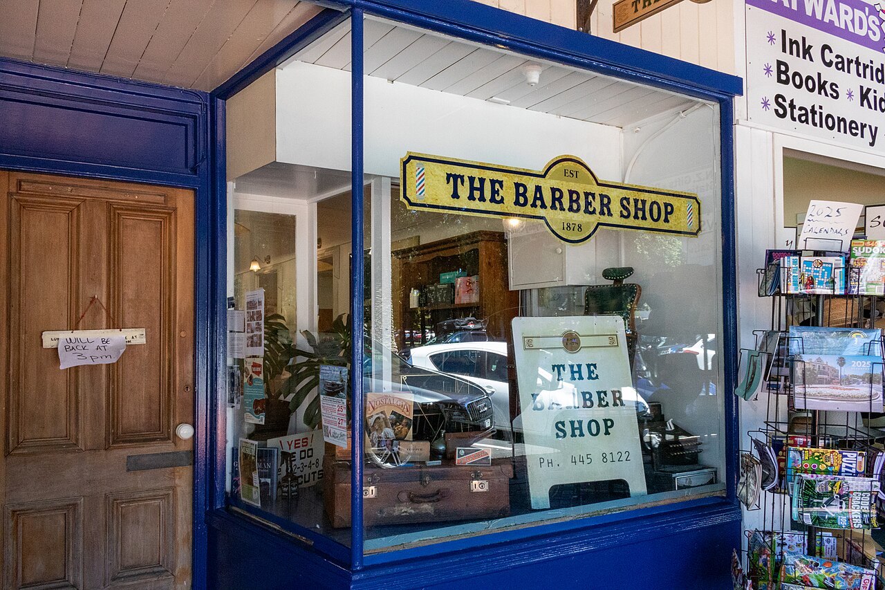 Vitrine d’un barbier avec une enseigne jaune The Barber Shop et un panneau avec le numéro de téléphone.